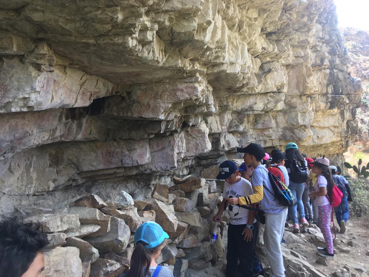Estudiantes de colegio observando pinturas rupestres precolombinas en el muro de las pictografías de Sáchica con Awalí School.
