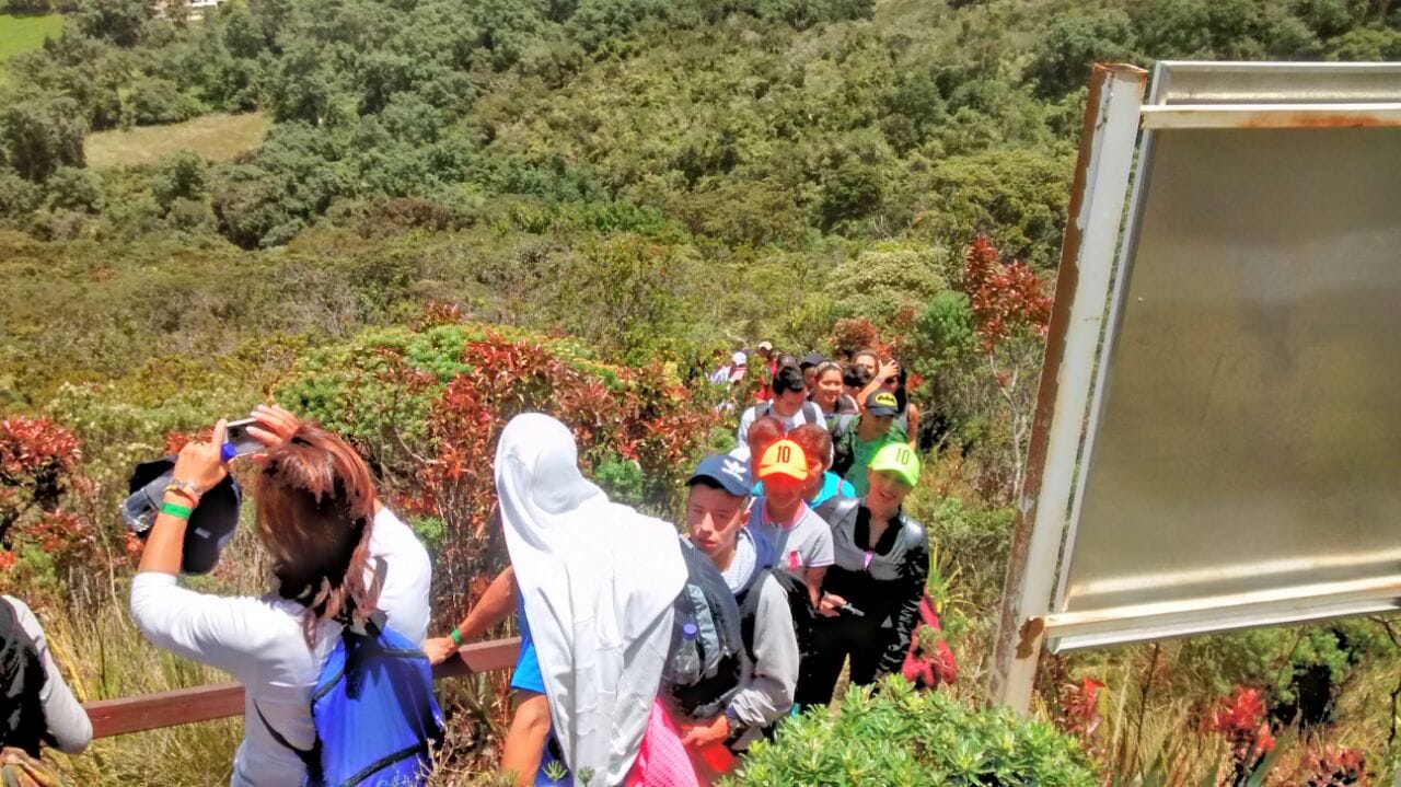 Staff de Awalí School brindando apoyo a estudiantes en un tramo húmedo del sendero hacia la Laguna de Guatavita, garantizando seguridad en áreas silvestres.